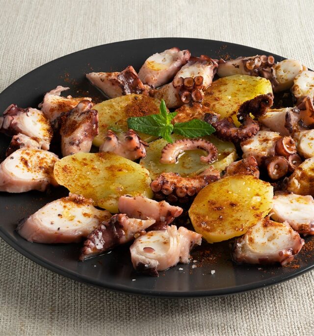 Delicious Pulpo a la Gallega: Traditional Spanish octopus dish with tender octopus slices, drizzled with olive oil, sprinkled with smoky paprika, and served on a bed of boiled potatoes.