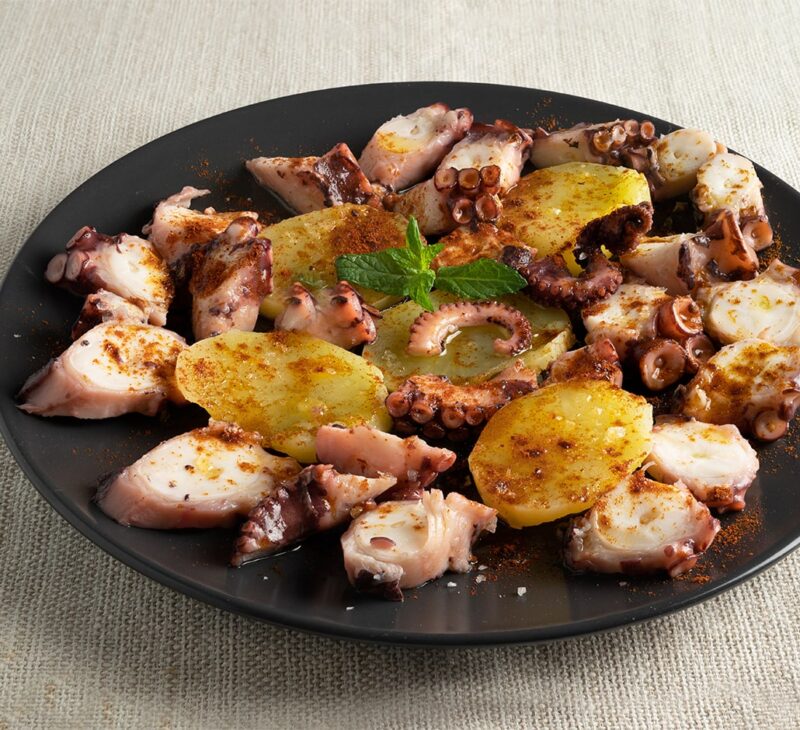 Delicious Pulpo a la Gallega: Traditional Spanish octopus dish with tender octopus slices, drizzled with olive oil, sprinkled with smoky paprika, and served on a bed of boiled potatoes.