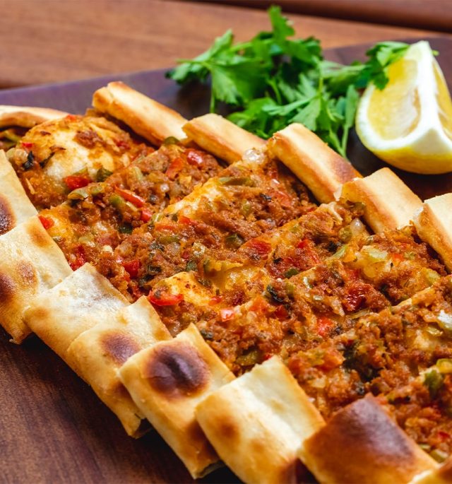 side view pide with ground meat tomato onion hot green pepper greens slice lemon tray