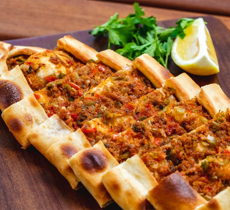 side view pide with ground meat tomato onion hot green pepper greens slice lemon tray